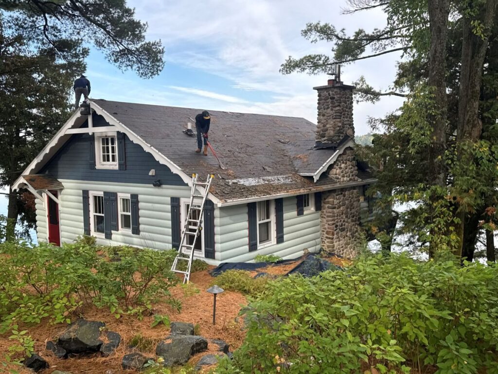 roofers inspecting and cleaning the roof of a house that is surrounded by trees