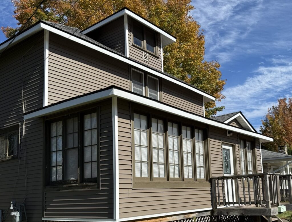 New siding on a large house, fall foliage in the background