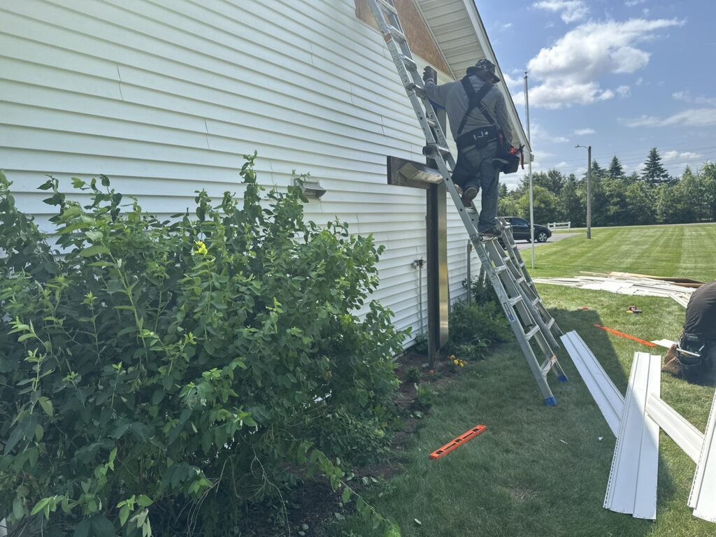 siding repair worker repairing siding on top of a ladder